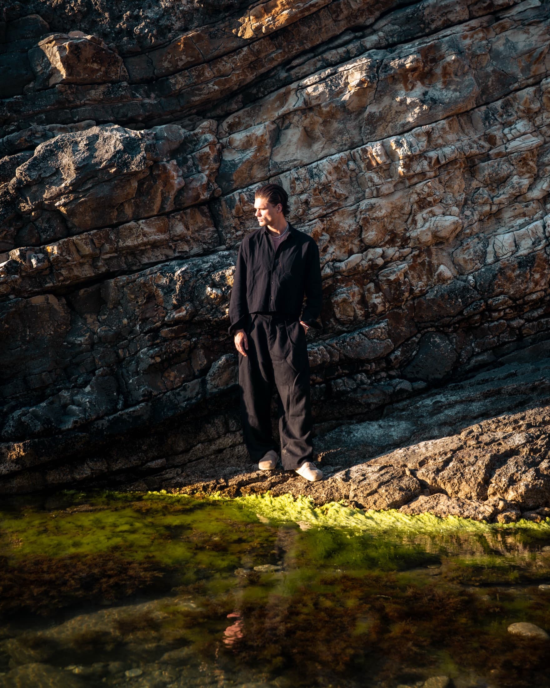A figure on dark wet rocks in golden light