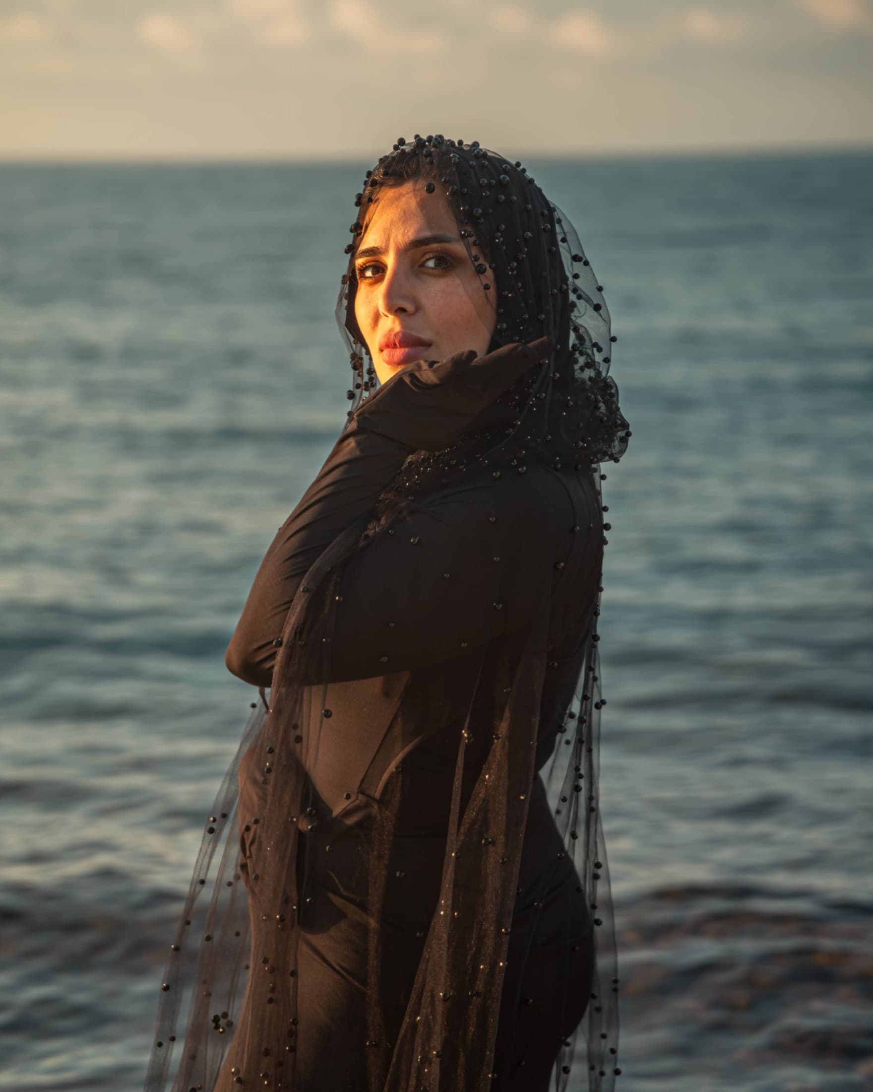 A figure in a black veil at the sea at sunset